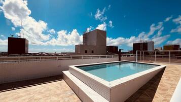 Una piscina en la azotea con vistas despejadas del horizonte urbano y un cielo azul.