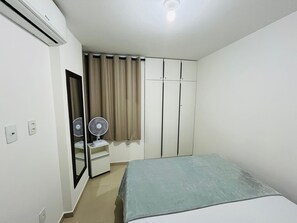 Un dormitorio con cama, armario, espejo, ventilador y lámpara en el techo.