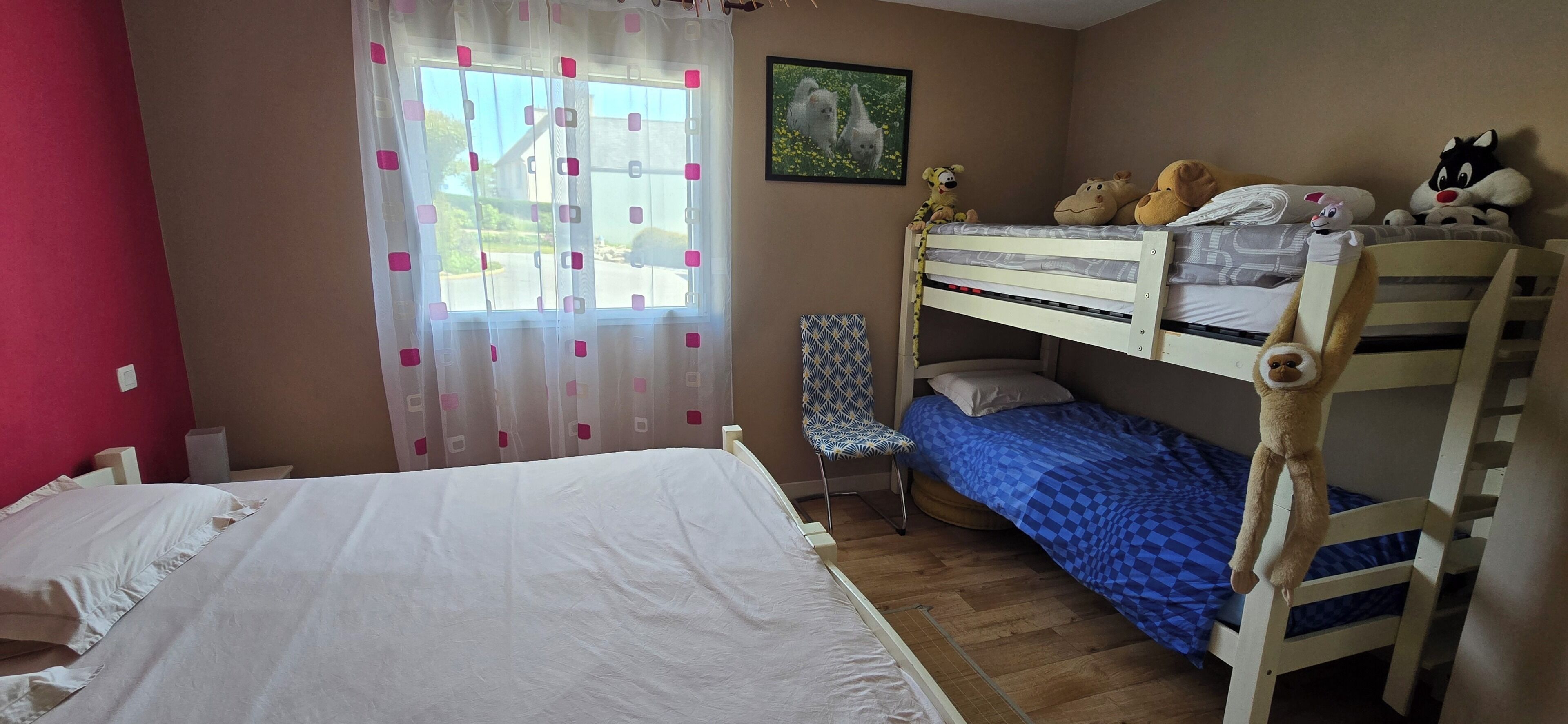 A room with a bunk bed, a single bed, a chair, and a window with curtains.