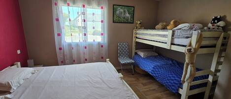 A room with a bunk bed, a single bed, a chair, and a window with curtains.