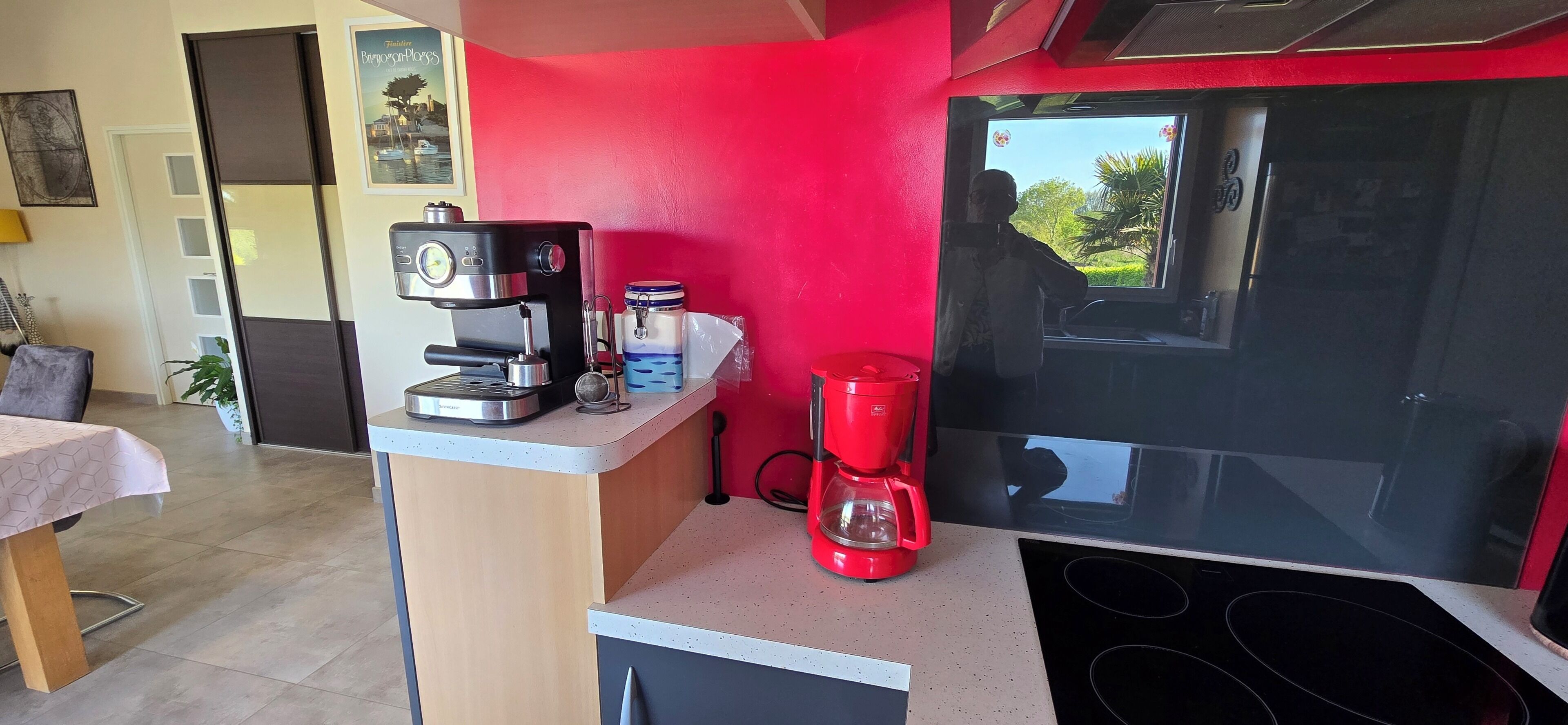 Una cucina con una macchina del caffè, una caffettiera rossa e un forno a microonde. Si vede una finestra con vista sul verde.