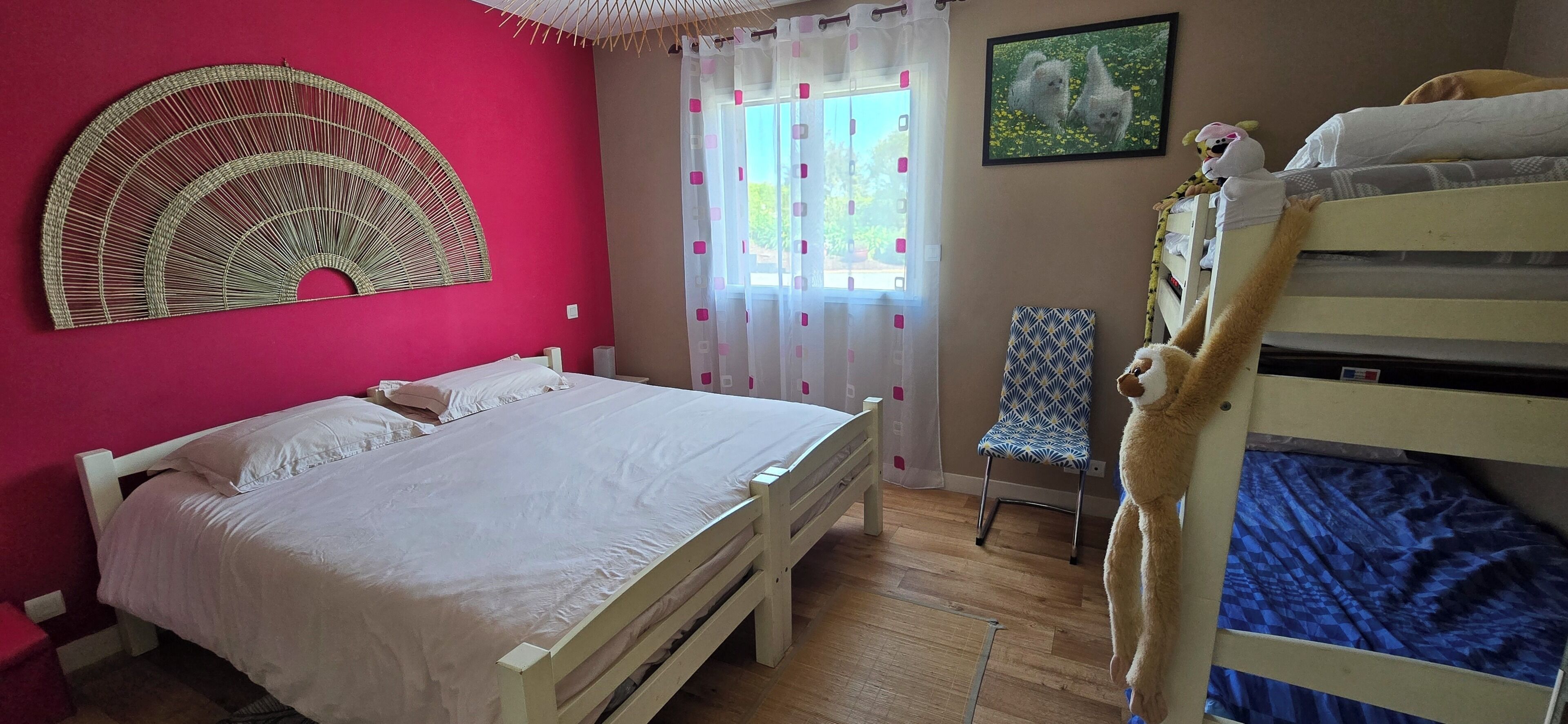 Una habitación con cama, silla, literas, un adorno en la pared y ventana con cortinas.