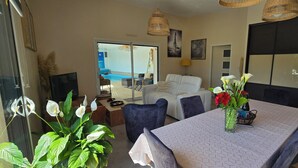 Comedor con mesa, sillas, un florero con flores y vista a una piscina y zona de estar exterior.