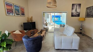 Una sala de estar con televisión, sofá y vista a una piscina a través de una puerta de cristal.