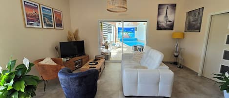 A living room with a television, sofa, and a view of a pool through a glass door.