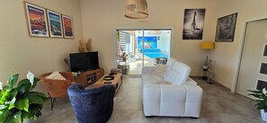 Ein Wohnzimmer mit Fernseher, Sofa und Blick auf ein Schwimmbad durch eine Glastür.
