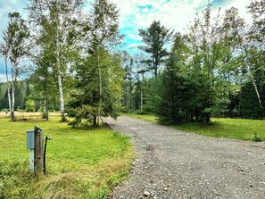 A gravel path in a wooded area with trees and a wooden post with a metal box. - Junction 19 & Co. - Upper Site #1 - RV & Tents with 50amp service - On Trails (Fort Kent)