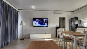A modern living room with a flat-screen TV mounted on the wall, a wooden dining table, and a kitchen area with a microwave and refrigerator. -     Luxury Ocean View Condo in Sosua Ocean Village (Sosúa)