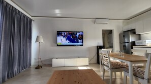 Ein modernes Wohnzimmer mit Wand-Fernseher, einem Holzesstisch und einer Küchenzeile mit Mikrowelle und Kühlschrank.