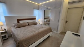 A bedroom with a bed, bedside lamp, nightstand, and a wardrobe with a mirror. -     Luxury Ocean View Condo in Sosua Ocean Village (Sosúa)