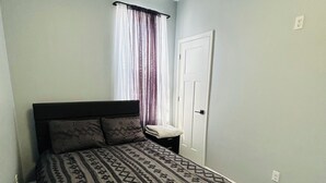 A bedroom with a bed, a nightstand, a door, and a window with curtains. - Wonderful two story, 2-bedroom apartment with AC in vibrant Detroit (Detroit)