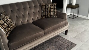 A brown tufted sofa with two patterned pillows, a dark patterned rug, and a potted plant on a small table beside it. - Wonderful two story, 2-bedroom apartment with AC in vibrant Detroit (Detroit)