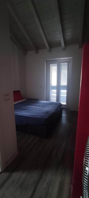 Um quarto com uma cama, uma janela com persianas e uma parede vermelha.