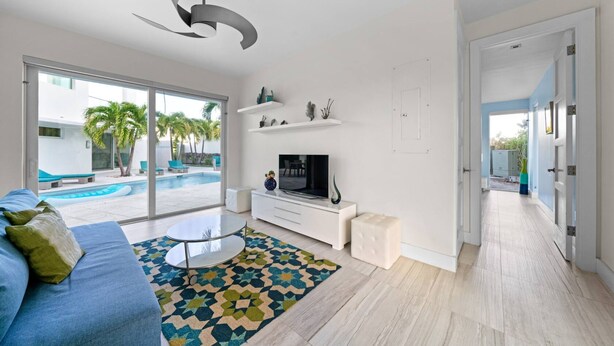 A modern living room with a TV, sofa, and a view of a swimming pool. - Luxury Pool Villa Steps From Stunning Beach Beautiful Views EAST TOWER ONLY (Moss Town)