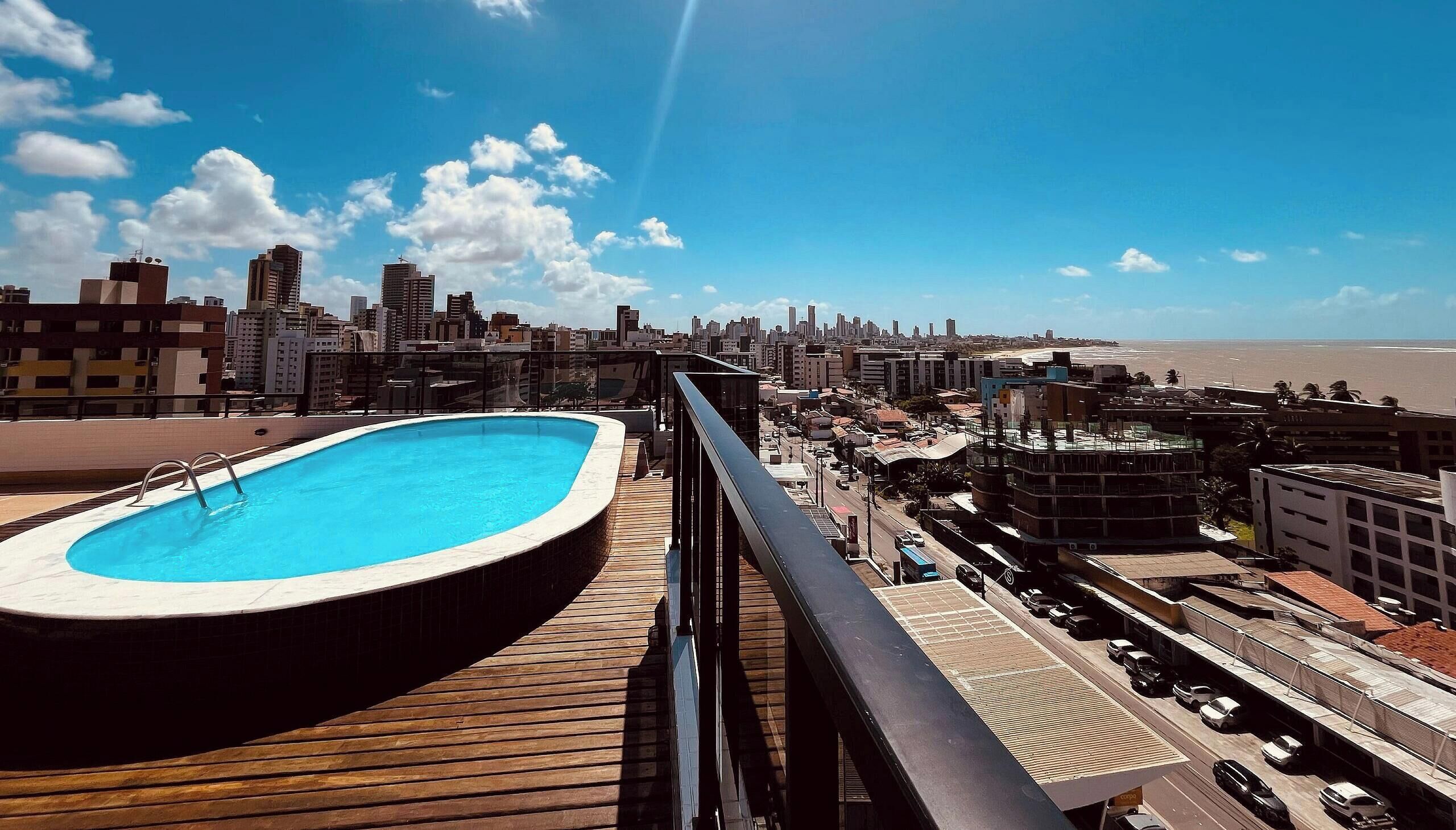 Una piscina en la azotea con vistas a la ciudad, una terraza de madera y cielo despejado.