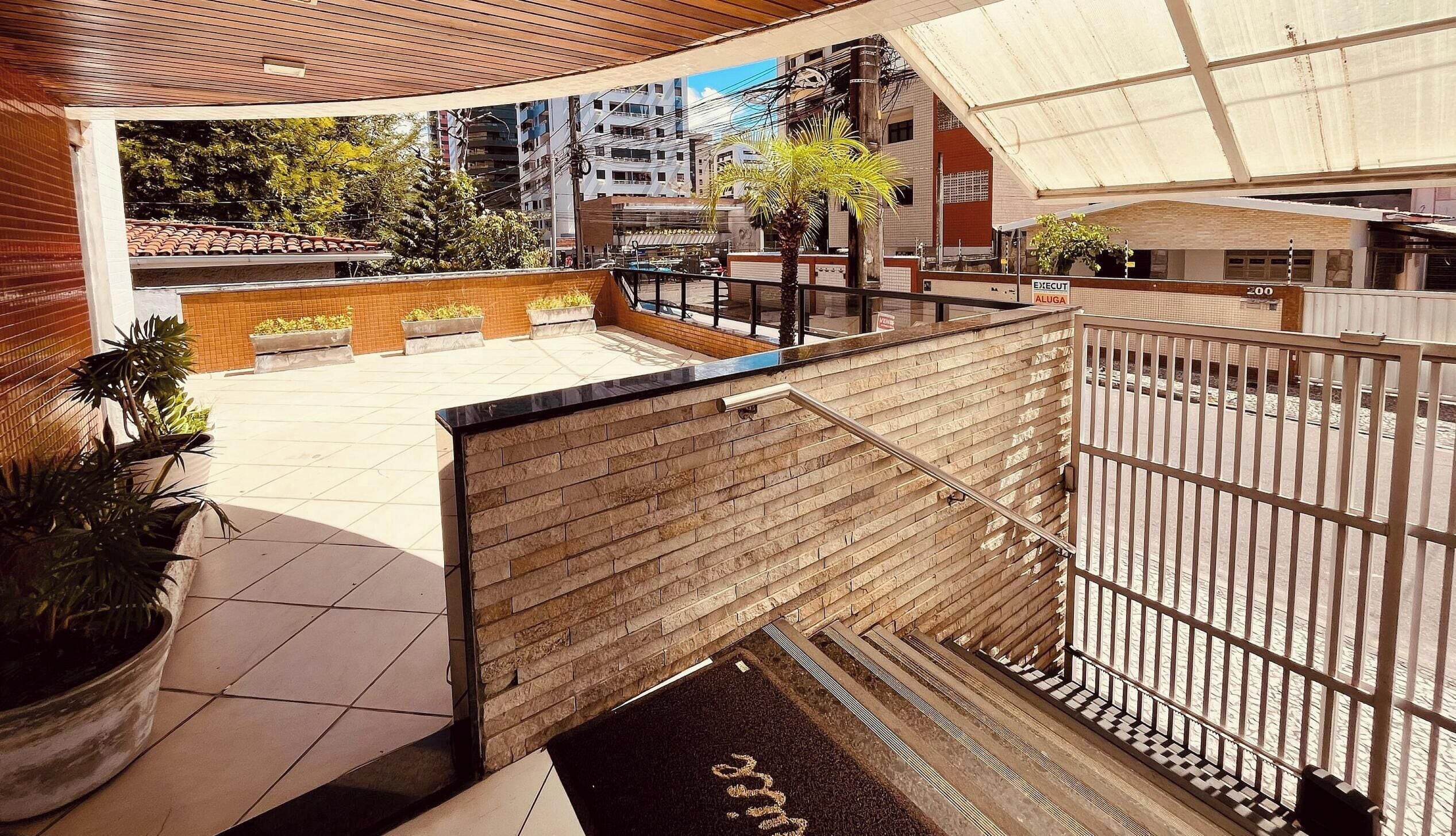 Terraza en la azotea con plantas en macetas, pared de ladrillo y baranda metálica.
