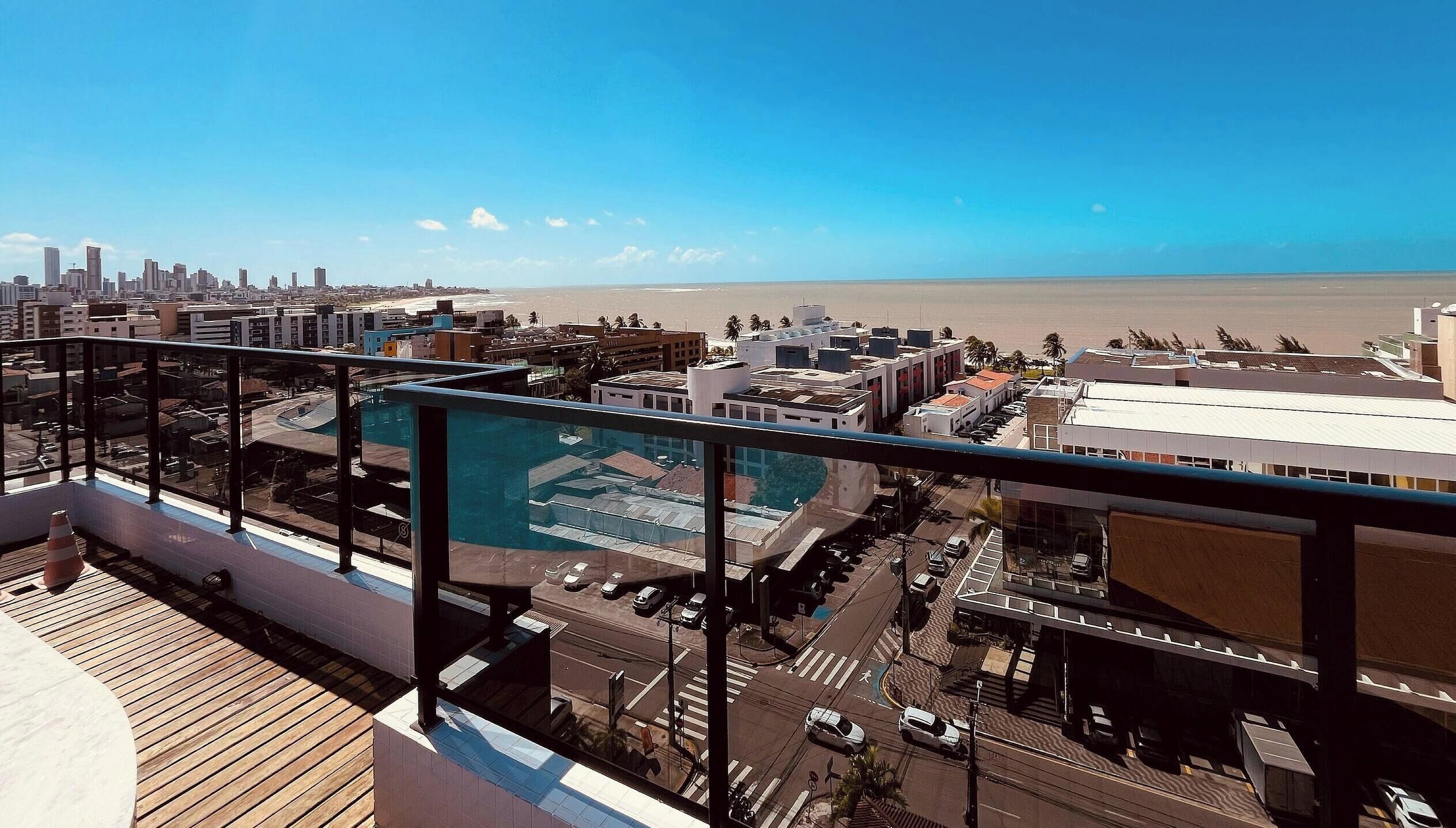 A high-rise building with a rooftop pool, a view of the cityscape, and a beach in the distance.
