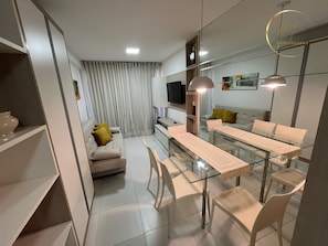 Un salón moderno con una mesa de comedor de vidrio, sofá blanco y una televisión de pantalla plana.