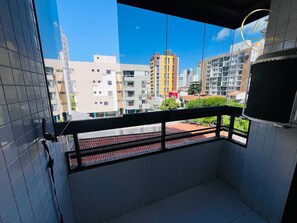 Un balcón con vistas a edificios urbanos, una pared con baldosas y una ventana con reja de metal.