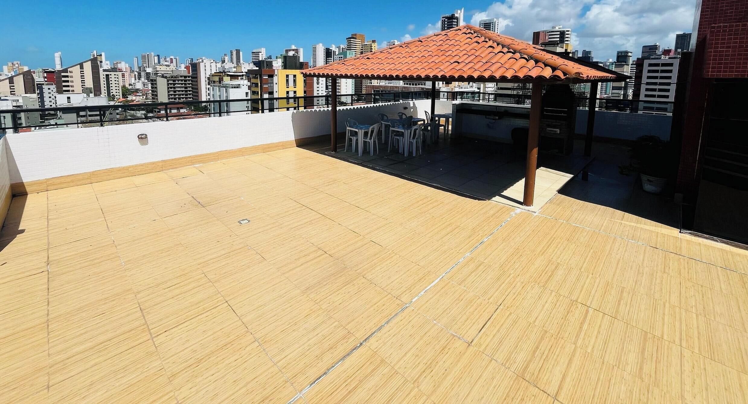 Una terraza en la azotea con piso de madera, un área de descanso cubierta y un horizonte urbano de fondo.