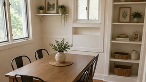 Et spiseområde med et træbord og stole, en potteplante på bordet og en reol med dekorative genstande.