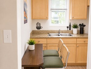 Een keuken met houten kastjes, een granieten aanrecht, een spoelbak, een eettafel met een stoel en een kamerplant.