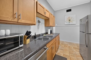 A kitchen with wooden cabinets, a granite countertop, stainless steel appliances, and a wall-mounted light fixture.