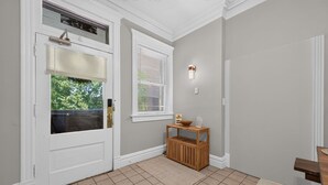 Ein Flur mit einer weißen Tür, einem Fenster mit Jalousien, einer hölzernen Bank und einer Wandleuchte.
