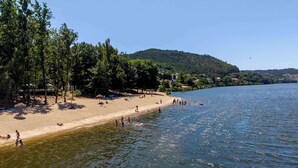 Una playa con gente nadando y tomando el sol, rodeada de árboles y colinas.
