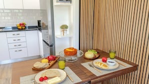 Una mesa de madera con un bol de fruta, un pastel y diferentes productos para el desayuno.