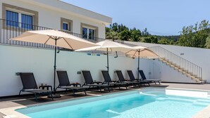 Piscina con sillones de descanso y sombrillas, una escalera y un edificio con ventanas.