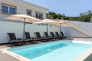 Ein Schwimmbecken mit Liegestühlen und Sonnenschirmen, eine Treppe und ein Gebäude mit Fenstern.