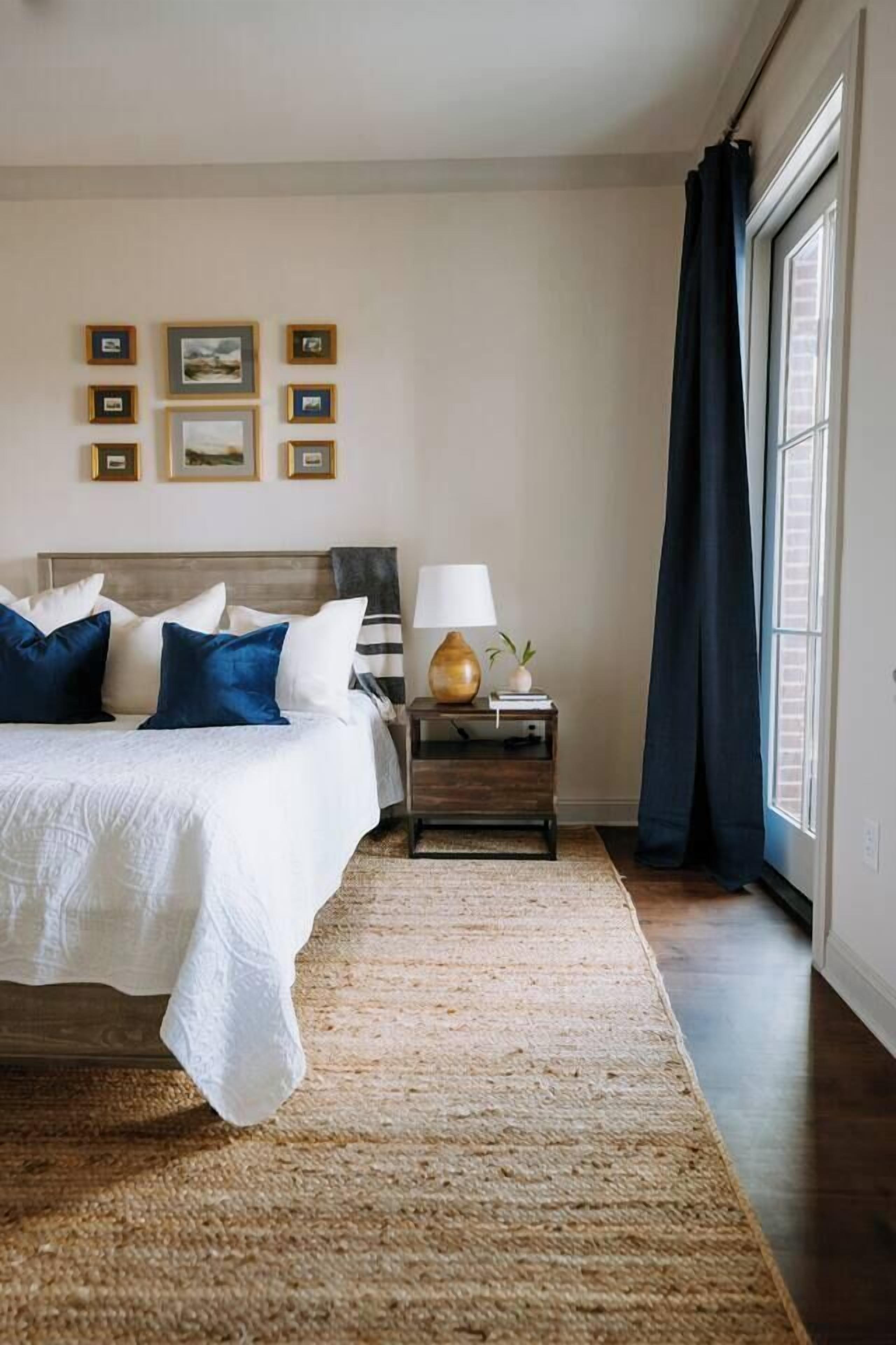 Un dormitorio con cama, mesita de noche, lámpara y cuadros en la pared.