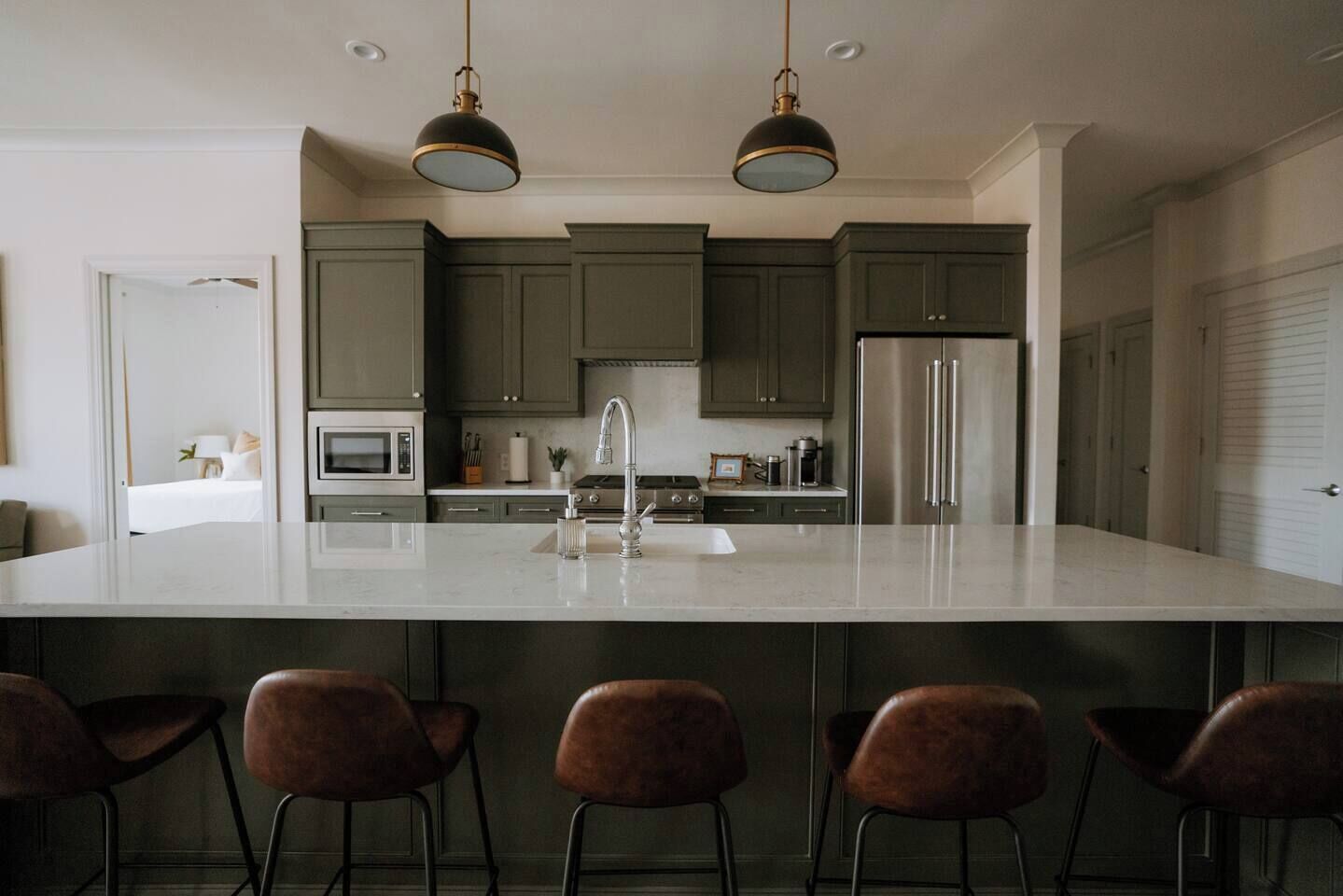 A modern kitchen with a large island, stainless steel appliances, and dark green cabinets.