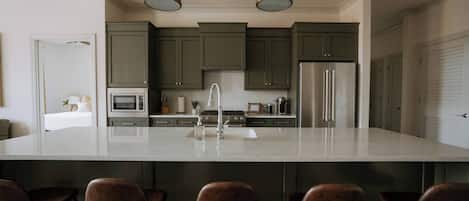 Uma cozinha moderna com uma ilha grande, eletrodomésticos de aço inoxidável e armários verde-escuro.