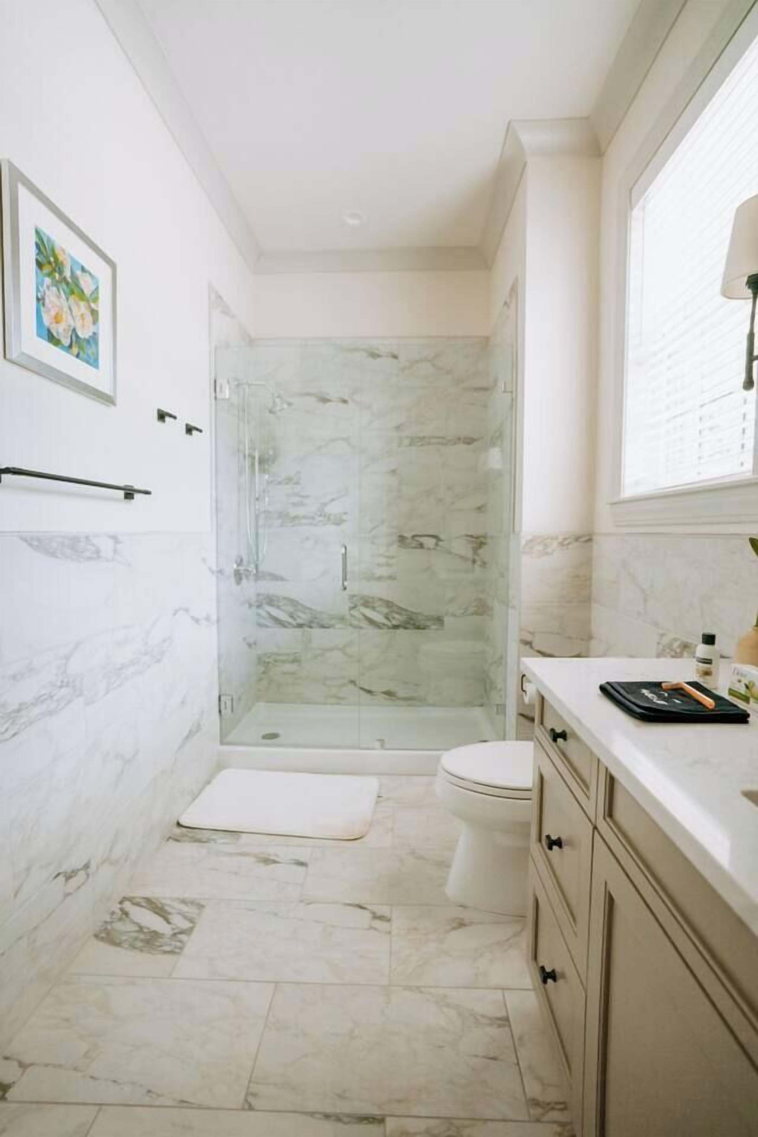 A bathroom with a glass-enclosed shower, a toilet, and a vanity with drawers.