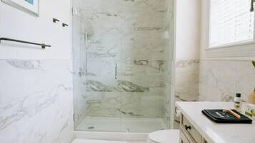 A bathroom with a glass-enclosed shower, a toilet, and a vanity with drawers.