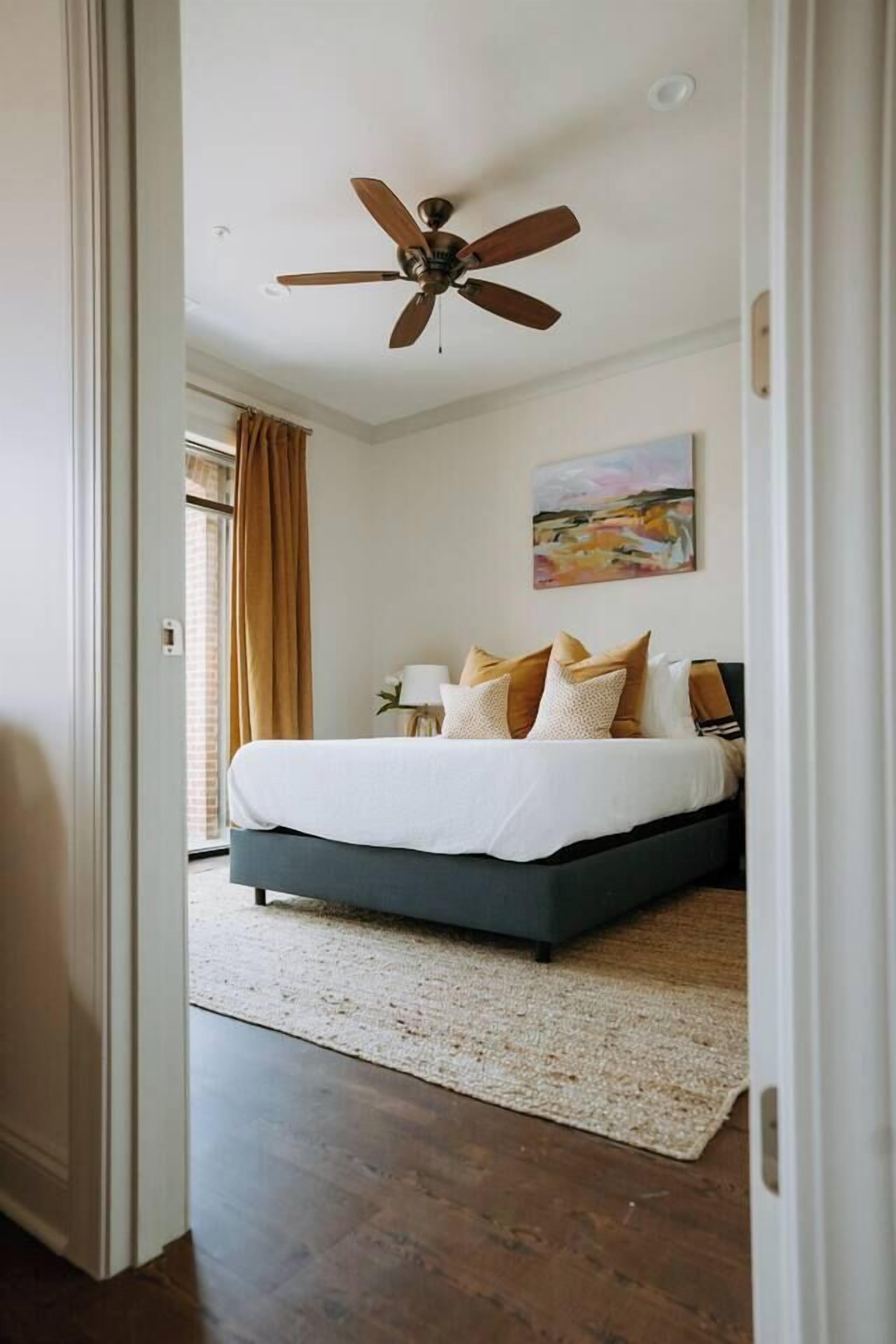 A bedroom with a bed, a ceiling fan, a painting, and a view through an open door.