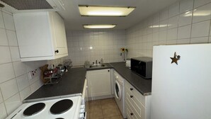 A compact kitchen with white cabinets, a microwave, a stove, and a washing machine. - Charming flat for short-term rent on a quiet,well-kept street close to Hyde Park (London)