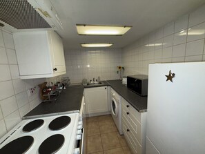 Eine kleine Küche mit weißen Schränken, einer Mikrowelle, einem Herd und einer Waschmaschine.