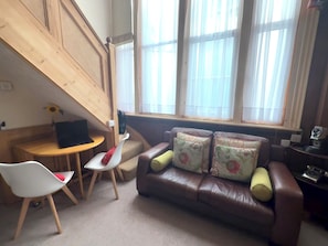 A cozy living area with a brown leather sofa, a white chair, a small wooden table, and a window with sheer curtains. - Charming flat for short-term rent on a quiet,well-kept street close to Hyde Park (London)
