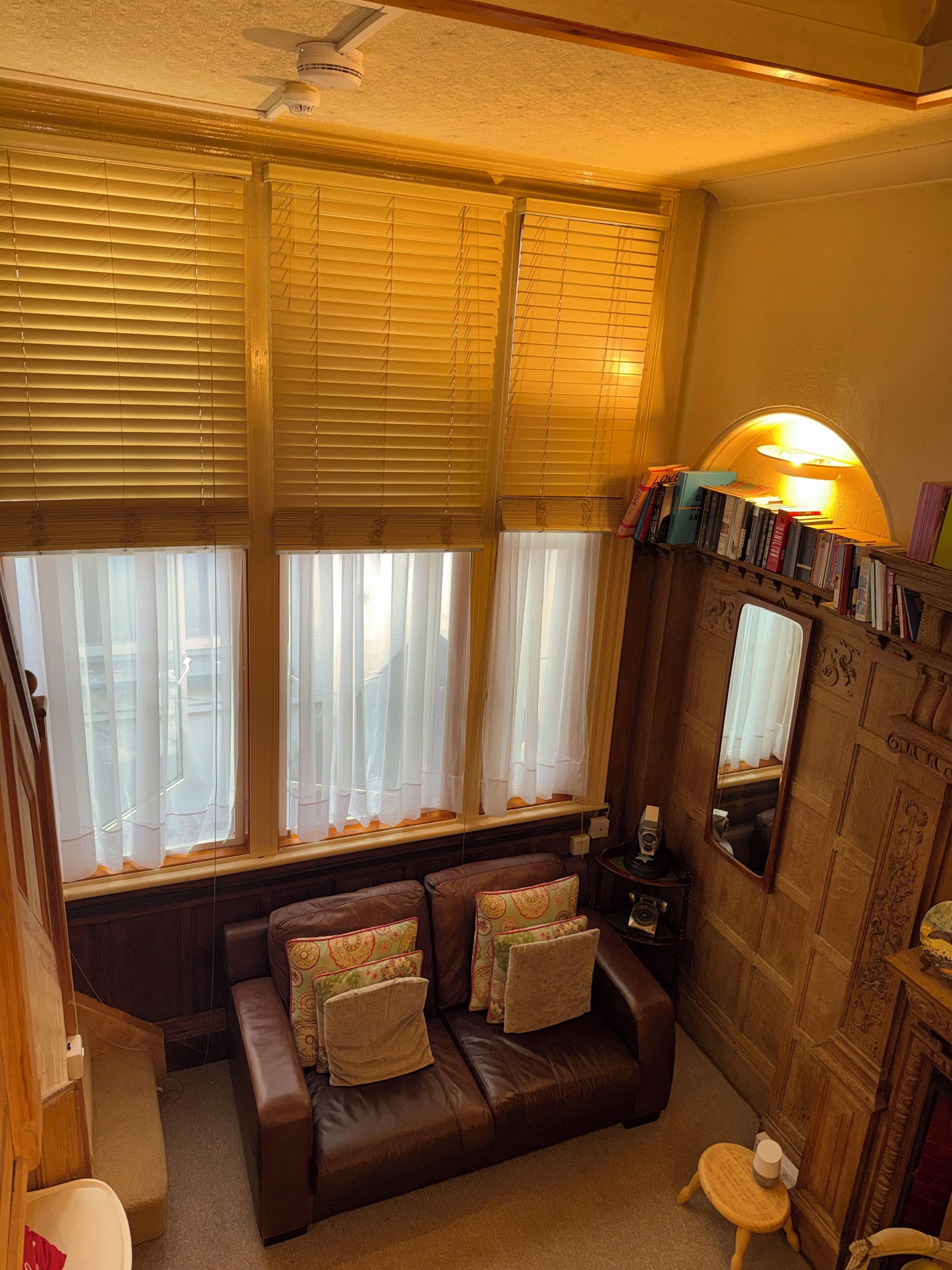 Een gezellige kamer met een bruine leren bank, een houten bijzettafeltje en een boekenplank vol boeken.