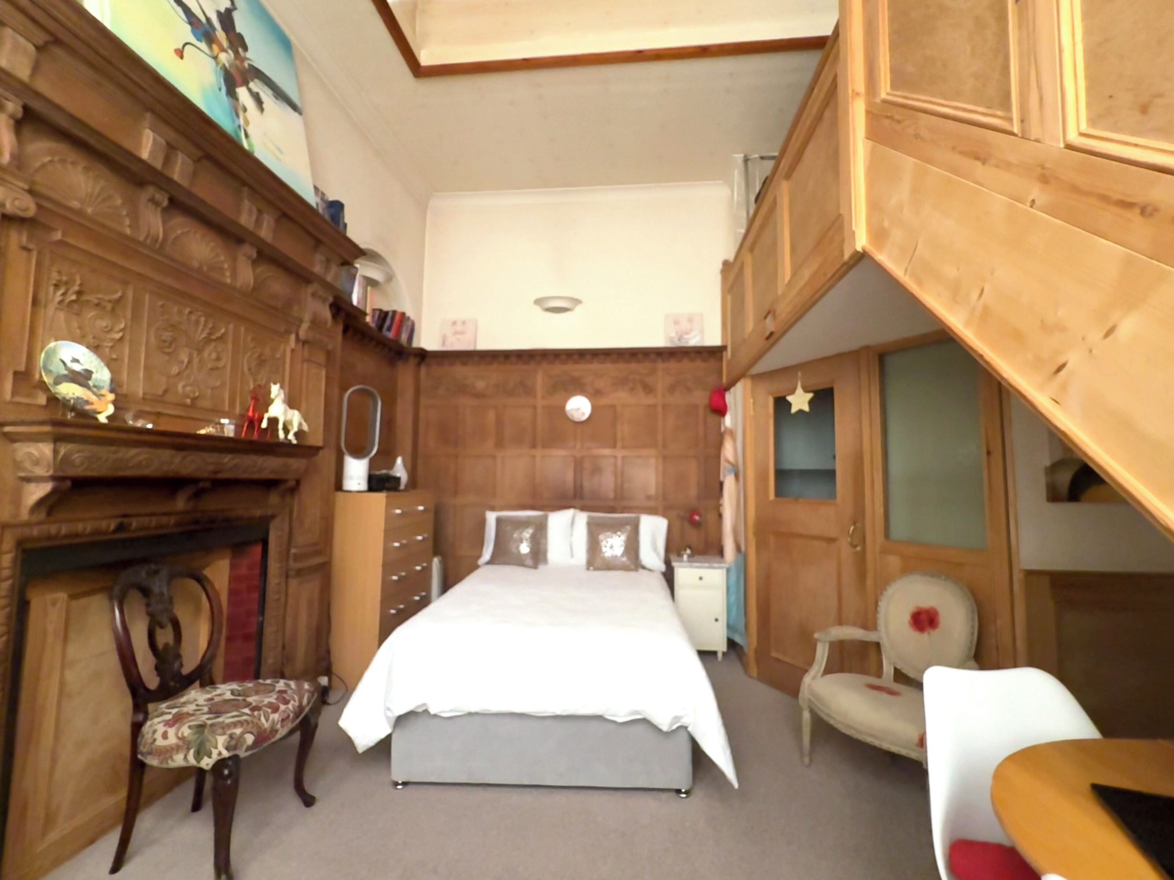 Een slaapkamer met een bed, een stoel, een dressoir en een spiegel.
