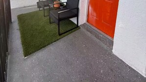 En balkong med en röd dörr, ett fönster, ett litet bord med två stolar och en krukväxt.
