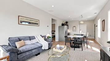 A modern living room with a grey sofa, a glass coffee table, and a dining area with a white table and chairs.