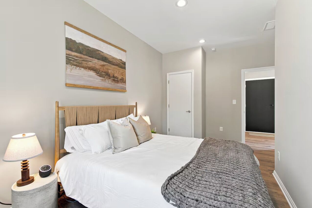 A bedroom with a bed, bedside lamp, and a painting on the wall.