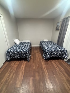 A room with two beds, wooden flooring, and a single wall with a picture.