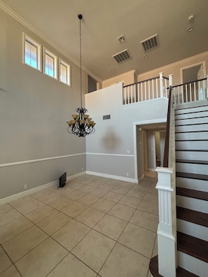 A spacious room with a chandelier, a staircase, and a view of the upper floor.