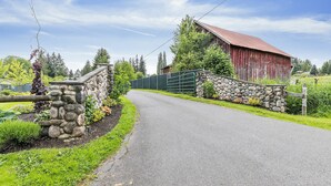 Un camino rural que lleva a un granero rojo con un muro de piedra y una reja de metal.