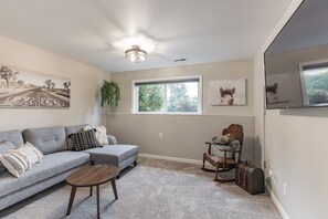 A living room with a sectional sofa, a small wooden table, a rocking chair, a potted plant, and a suitcase. - Peaceful 1-bedroom apartment with private entry in charming Snohomish (Snohomish)
